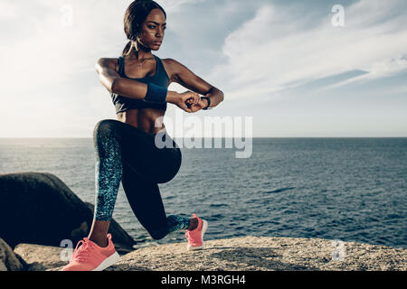 Afrikanische Frau tun Stretching Übungen am Strand. Weibliche tun Aufwärmen erstreckt sich auf den Felsen am Strand. Stockfoto