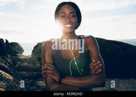Portrait von gesunde Frau Entspannung nach dem Training im Freien. Fitness Frau steht auf Felsen mit verschränkten Armen und lächelnd. Stockfoto