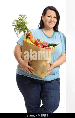 Übergewichtige Frau mit einer Papiertüte mit Gemüse und Obst gegen eine Wand auf weißem Hintergrund schiefen gefüllt Stockfoto