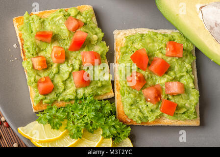 Von oben nach unten von Sandwiches mit mexikanische Soße guacamole mit Avocado, gehackte Tomaten und weißes Brot Toast dekoriert Alligator Pear Frucht, in Scheiben geschnittenen Zitrone Stockfoto