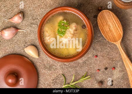 Von oben nach unten von Fischsuppe mit Stör, Kartoffeln in Ton Platte, dekoriert mit Knoblauch, Rosmarin Blätter, Roggen Brot und Löffel aus Holz auf Stein Hintergrund Stockfoto