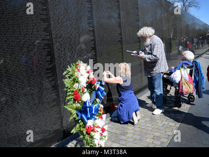 Auf nationaler Vietnam Veterans Day, Familienmitglieder, Touristen und Besucher zu Washington D.C. zahlen ihren Respekt für die gefallenen Helden des Vietnam Krieges am Denkmal der Vietnam Veteran auf der National Mall entfernt. Die Mauer der Erinnerung besteht aus zwei 246 Fuß 9 Zoll (75.21 m) langen gabbro Wänden aus, mit den Namen der Soldaten in horizontalen Zeilen mit regelmäßigen Schrift und Zeilenabstand geehrt wird geätzt. Die Wände sind in den Boden versenkt, mit der Erde hinter Ihnen. Auf der höchsten Spitze (apex, wo Sie sich treffen), sind sie 10,1 Fuß (3,1 m) hoch, und sie zu einer Höhe von 8 inkl Konus Stockfoto