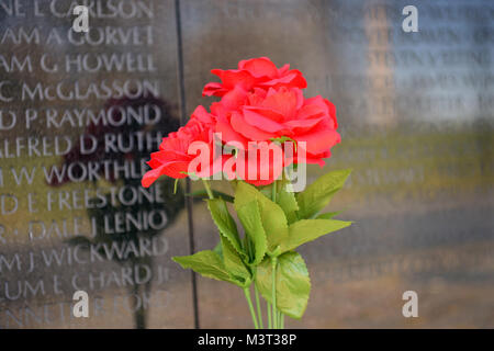 - Auf nationaler Vietnam Veterans Day, einige verlassen Blumen, einige verlassen Flags als Familienmitglieder, Touristen und Besucher zu Washington D.C. zahlen ihren Respekt für die gefallenen Helden des Vietnam Krieges am Denkmal der Vietnam Veteran auf der National Mall entfernt. Die Mauer der Erinnerung besteht aus zwei 246 Fuß 9 Zoll (75.21 m) langen gabbro Wänden aus, mit den Namen der Soldaten in horizontalen Zeilen mit regelmäßigen Schrift und Zeilenabstand geehrt wird geätzt. Die Wände sind in den Boden versenkt, mit der Erde hinter Ihnen. Auf der höchsten Spitze (apex, wo Sie sich treffen), sind sie 10,1 Fuß (3,1 m Stockfoto