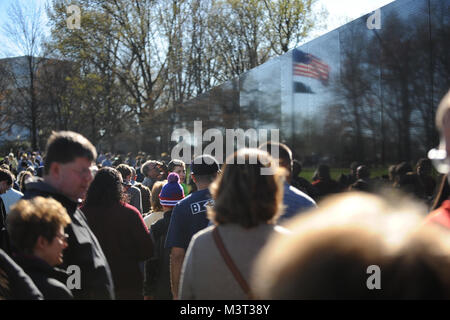 Auf nationaler Vietnam Veterans Day, Familienmitglieder, Touristen und Besucher zu Washington D.C. zahlen ihren Respekt für die gefallenen Helden des Vietnam Krieges am Denkmal der Vietnam Veteran auf der National Mall entfernt. Die Mauer der Erinnerung besteht aus zwei 246 Fuß 9 Zoll (75.21 m) langen gabbro Wänden aus, mit den Namen der Soldaten in horizontalen Zeilen mit regelmäßigen Schrift und Zeilenabstand geehrt wird geätzt. Die Wände sind in den Boden versenkt, mit der Erde hinter Ihnen. Auf der höchsten Spitze (apex, wo Sie sich treffen), sind sie 10,1 Fuß (3,1 m) hoch, und sie zu einer Höhe von 8 inkl Konus Stockfoto