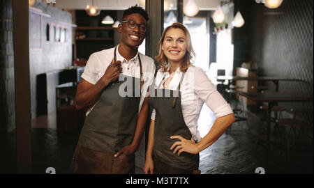 Glückliche junge Coffee shop besitzer stehen an ihrem Geschäft. Mann und Frau baristas im Café tragen Schürze. Stockfoto