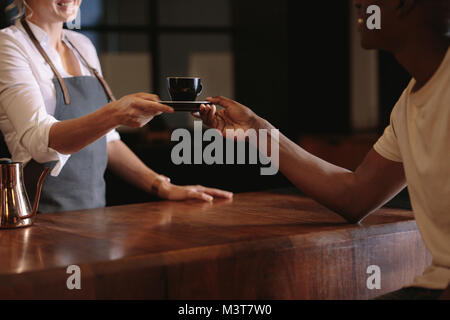 Mit Frau Kaffee über den Zähler an einen Kunden. 7/8-Schuss von Kaffee shop besitzer übergeben, um eine Tasse Kaffee zu ihren Kunden. Stockfoto