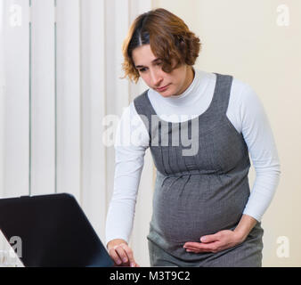 Junge schwangere Frau im Kleid, die im Büro arbeiten Stockfoto