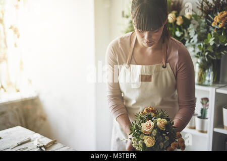 Junge Frau einen Blumenstrauß aus gemischten Blumen, während an einem Tisch in Ihrem Blumenladen arbeiten Stockfoto