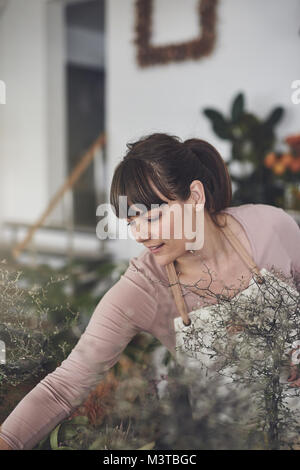 Lächelnde junge weibliche florist Anordnen von Pflanzen auf einer Tabelle anzeigen, während Beschäftigte arbeitet sie in ihrem Blumenladen Stockfoto