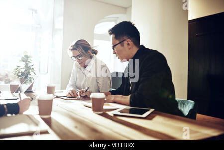 Zwei verschiedene Kollegen zusammen an einem Tisch arbeiten in einem modernen Büro Schreibarbeit diskutieren Stockfoto
