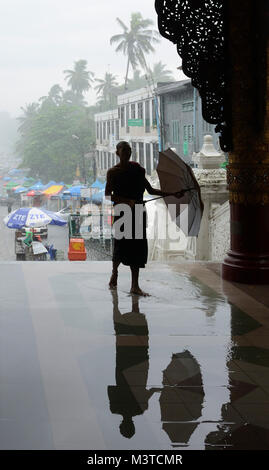 Mönch am Eingang zur Shwedagon Pagode an einem regnerischen Tag, Yangon, Myanmar Stockfoto