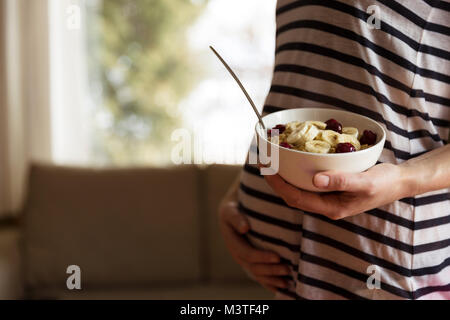 Schwangere Frau mit einer Schüssel mit einem gesunden Frühstück Haferbrei mit Früchten nach dem Workout. Gesunde Schwangerschaft Stockfoto