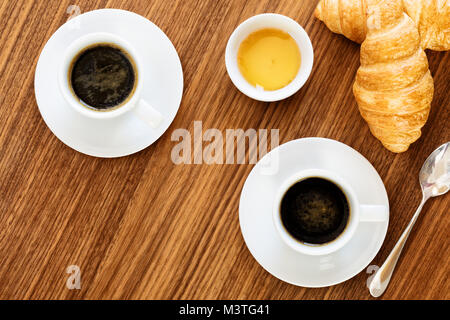 Zwei Tassen Kaffee mit Croissants, Honig und Tütchen Zucker auf Holztisch. top View Stockfoto