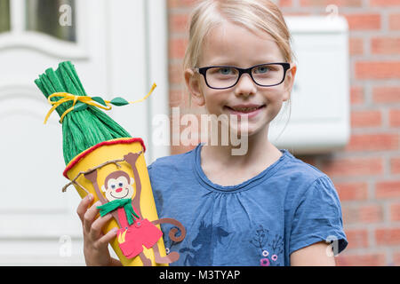 Ein blondes Mädchen in Gläsern freut sich auf seinen ersten Tag an der Schule und wirft mit der Schultasche vor der Haustür. Stockfoto