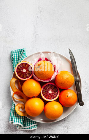 Eine Gruppe von Orangen auf einem Teller. Einige von ihnen geschnitten. Messer und Handtuch. Auf einem Stein Hintergrund. Eine gesunde Sommer Tabelle, die Vorbereitung von frisch gepressten j Stockfoto