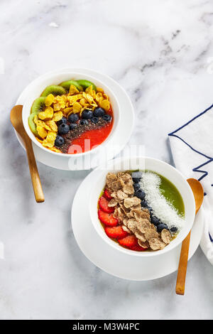 Zwei Schalen mit unterschiedlichen Smoothies aus Erdbeeren und Kiwis, mit Getreide für ein gesundes Frühstück und Beeren, Chia Samen und Kokos Chips mit Fre Stockfoto