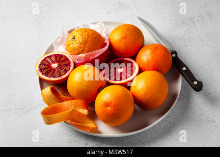 Eine Gruppe von Orangen auf einem Teller. Einige von ihnen geschnitten. Messer. Auf einem Stein Hintergrund. Eine gesunde Sommer Tabelle, die Vorbereitung von frisch gepressten Saft oder d Stockfoto