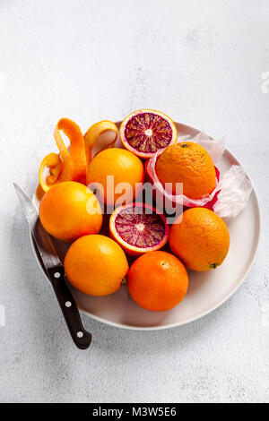 Eine Gruppe von Orangen auf einem Teller. Einige von ihnen geschnitten. Messer. Auf einem Stein Hintergrund. Eine gesunde Sommer Tabelle, die Vorbereitung von frisch gepressten Saft oder d Stockfoto