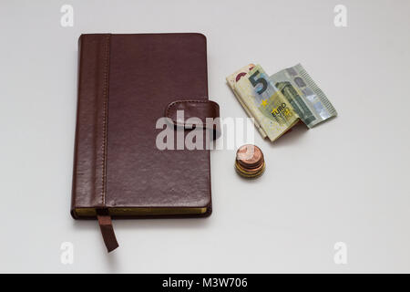 Hinweis Buch und Euro-Banknoten und -Münzen auf weißem Hintergrund Stockfoto