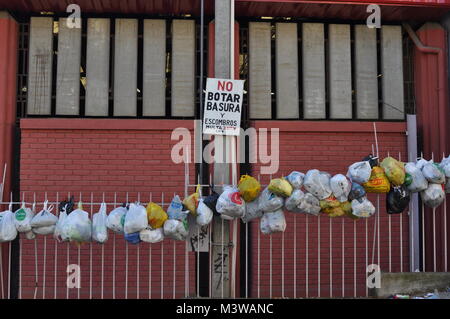 Säcke mit Müll an einem metallzaun vor einem 'Littering' Zeichen in Spanisch Stockfoto