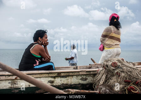 Zwei Frauen und ein Mann mit einem hölzernen Fischerboot am Strand in La Guajira, Kolumbien warten Stockfoto