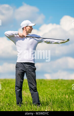 Männliche professioneller Golfspieler posiert mit einem Golf Club in ein grünes Feld im Sommer Stockfoto
