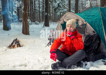 Aktive müde Frau sitzt in der Nähe von Zelt im Winter Wald Stockfoto