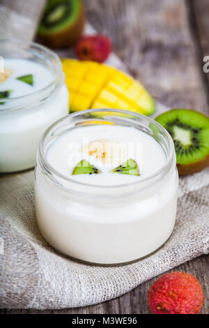 Joghurt mit tropischen Früchten auf einem hölzernen Hintergrund. Leckeres Frühstück. Das gesunde Essen. Stockfoto