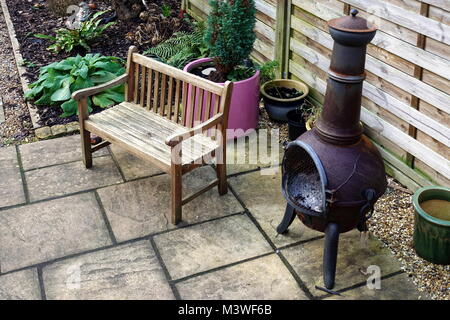 Holzbank, chiminea und verschiedene Pflanzen, einige in Töpfe, in einem kleinen heimischen Garten im Innenhof im Winter. Stockfoto