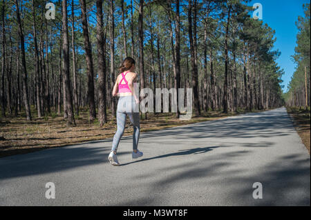 Frau Läufer, laufen entlang einer langen, geraden Straße durch einen Wald Stockfoto