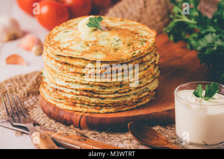 Viele Pfannkuchen mit frischen Kräutern und saure Sahne Soße auf einer hölzernen Tisch. Traditionelle ukrainische oder russische Pfannkuchen. Maslenitsa. Traditionelle Gerichte auf Th Stockfoto