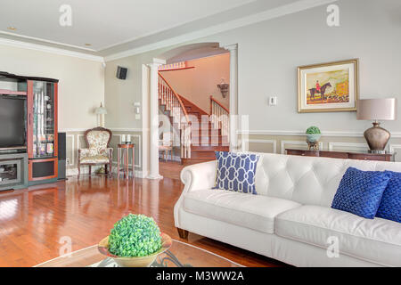 Weiß Wohnzimmer mit TV Regal, Stuhl und Tisch mit Pferd, Kunst an der Wand und der Blick durch den Bogen des eine gewundene Treppe, die Treppe Stockfoto