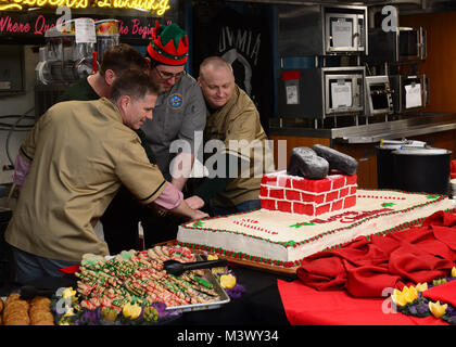 NAVAL BASE KITSAP Bremerton, Washington (31. 25, 2017) U.S. Navy Cmdr. J.W. David Kurtz, Executive Nimitz Officer's, Links, Kapitän Kevin Lenox, kommandierender Offizier der Flugzeugträger USS Nimitz (CVN 68), Mitte, kulinarische Specialist 2. Klasse Anthony Taylor, von Richmondville, Ga, Mitte und Nimitz's Command Master Chief, Jimmy Hailey, rechts, schneiden Sie einen Kuchen in ein Weihnachtsessen an Bord Nimitz (CVN 68), Dez. 25, 2017, im Marinestützpunkt Kitsap Bremerton. Der Nimitz befindet sich derzeit in der Vorbereitung für eine geplante schrittweise Verfügbarkeit Puget Sound Naval Shipyard und Intermediate Maintenance Facility, wo die Sh Stockfoto