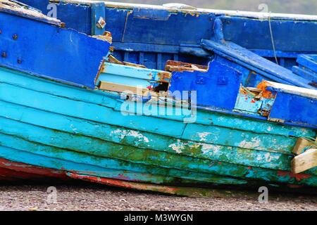 Völlig ruiniert und Holzboot mit hellen blauen Lackierung aufgegeben am Strand links oben zu brechen. Stockfoto