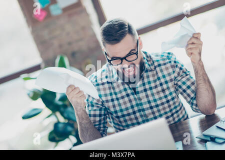 Deprimiert frustriert verrückt Freelancer in kariertem Hemd und Brille bekleidet am Tisch sitzt, die am Monitor auf seinem Laptop suchen, schreit Stockfoto