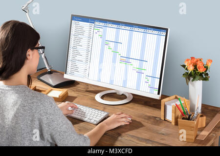 Junge Frau auf Gantt-diagramm mit Computer am Arbeitsplatz Stockfoto