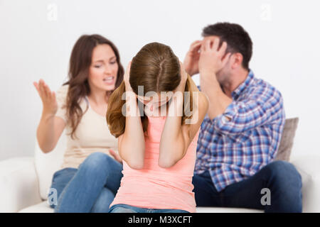 Eltern sitzen auf dem Sofa streiten Lautstark hinter Mädchen für Ihre Ohren Stockfoto