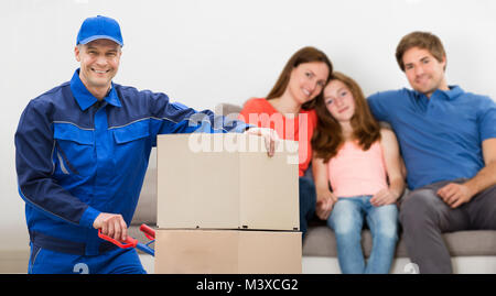 Happy Delivery Man mit Pappkartons Vor Familie sitzt auf einem Sofa Stockfoto