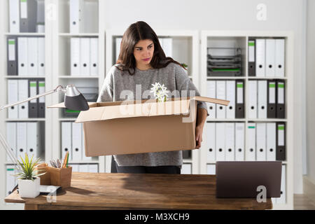 Unglückliche Junge Geschäftsfrau, die ihr Hab und Gut in Kartons am Arbeitsplatz Stockfoto