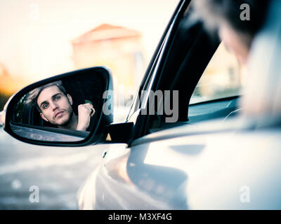 Schönen blonden jungen Mann, der ein Auto fährt, gesehen in der Rückspiegel Stockfoto