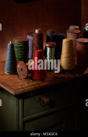 Mehrere weben Spulen mit Baumwolle oder Wolle thread auf Ihnen. Vertikale Farbfoto Schuß in einem Studio mit dramatische Beleuchtung. Dunklen Erdtönen Stockfoto