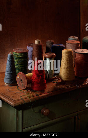 Mehrere weben Spulen mit Baumwolle oder Wolle thread auf Ihnen. Vertikale Farbfoto Schuß in einem Studio mit dramatische Beleuchtung. Dunklen Erdtönen Stockfoto