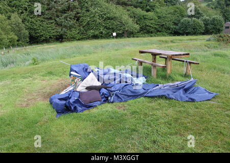 Abandonned, kollabierte blauen Zelt, Schlafsack und Camping Platz neben einem hölzernen Picknicktisch auf grünem Gras. Camping disater. Stockfoto