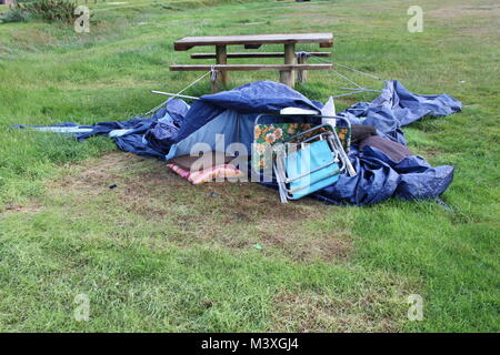 Abandonned, kollabierte blauen Zelt, Schlafsack und Camping Platz neben einem hölzernen Picknicktisch auf grünem Gras. Camping disater. Stockfoto