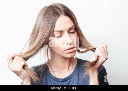 Strapaziertes Haar. Schöne traurige junge Frau mit langen Zerzausten Haaren. Closeup Portrait von weiblichen Modell Holding unordentlich Unbrushed trockenes Haar in den Händen. Haar Da Stockfoto