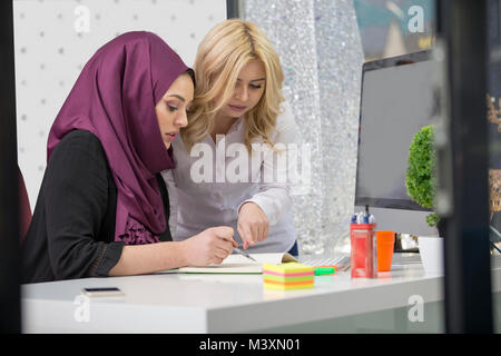 Europäische Frau und asiatischen muslimische Frau zusammen am gleichen Projekt Stockfoto