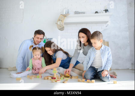 Eltern spielen mit ihren drei Kindern. Vater, Mutter, Sohn und zwei Töchter sitzen auf dem Boden im Zimmer. Alle zusammen bilden Sie etwas her Stockfoto