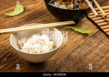 Asiatische Rindfleisch mit Gemüse und Reis auf schwarzem Teller und Essstäbchen Stockfoto