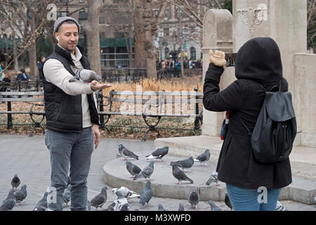 Ein Mann in Washington Square Park die Fütterung der Tauben und durch seine Begleiterin fotografiert werden. Stockfoto