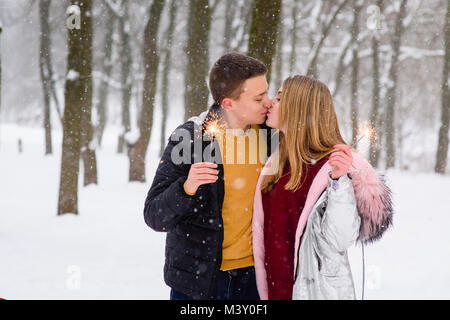 Romantische Kuss bei Schneefall im Winter Wald. Junges Paar mit Bengals im Freien. Stockfoto